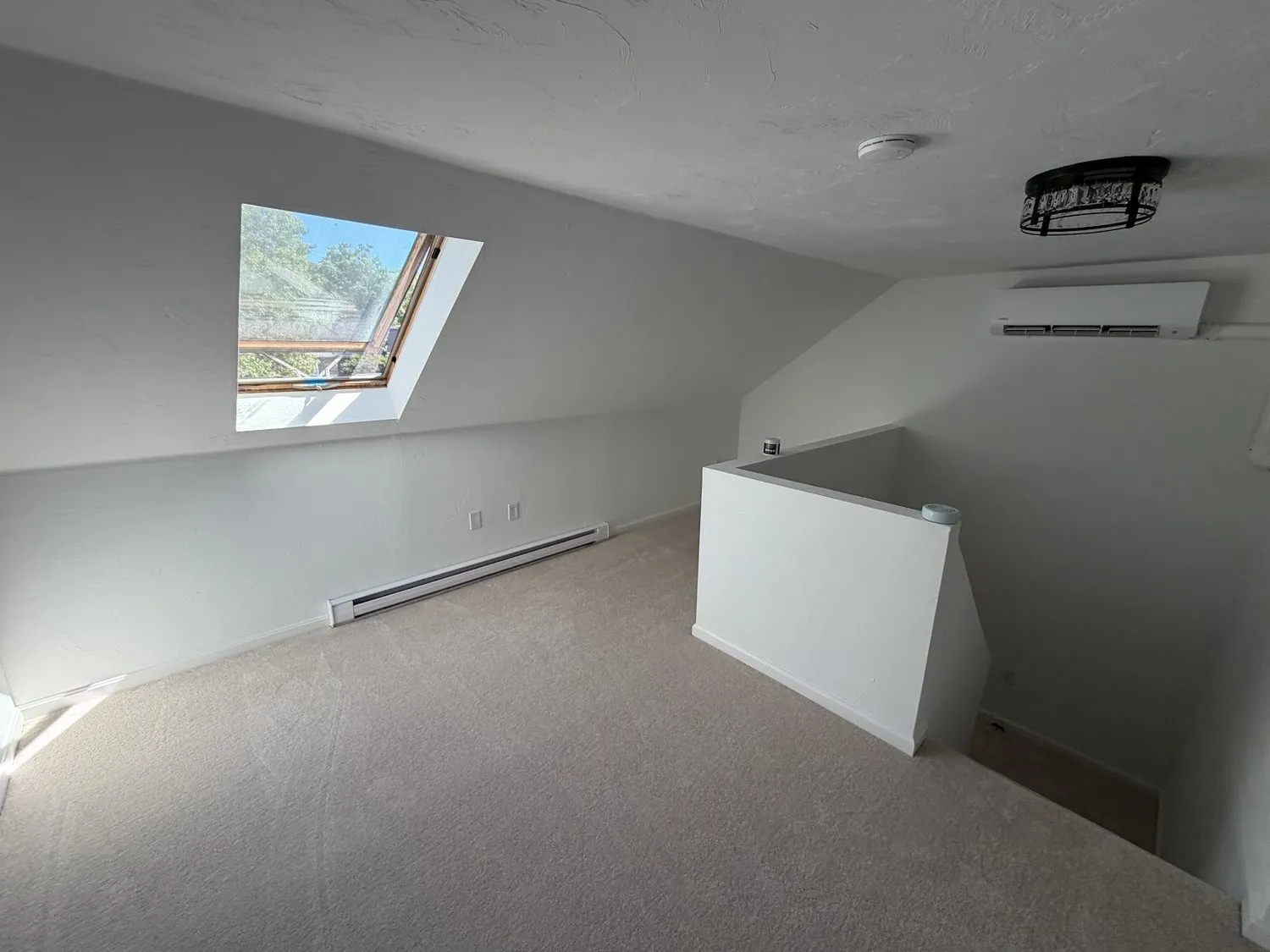 An attic room with sloped ceilings and a skylight, painted in soft gray and white