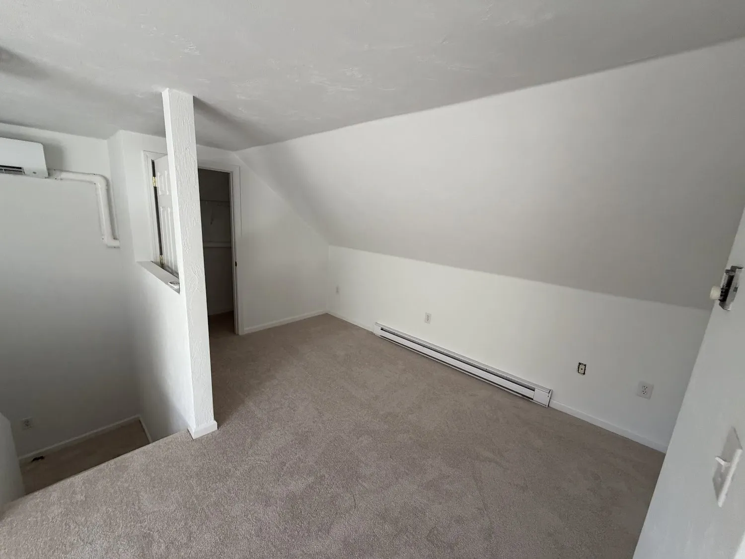 A sloped-ceiling attic room finished in white with a wall-mounted heating unit