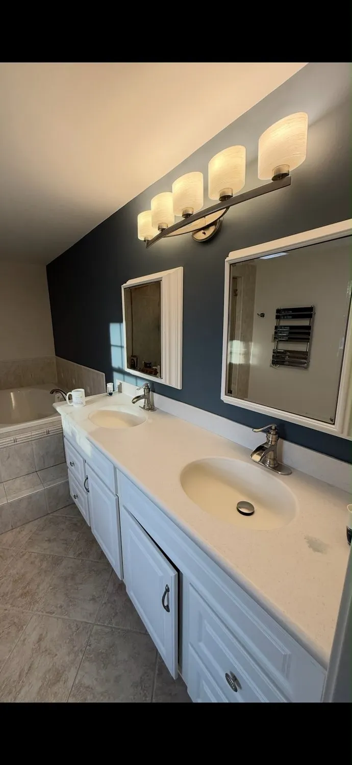 A bathroom with a dark navy wall, a white double vanity and two backlit mirrors