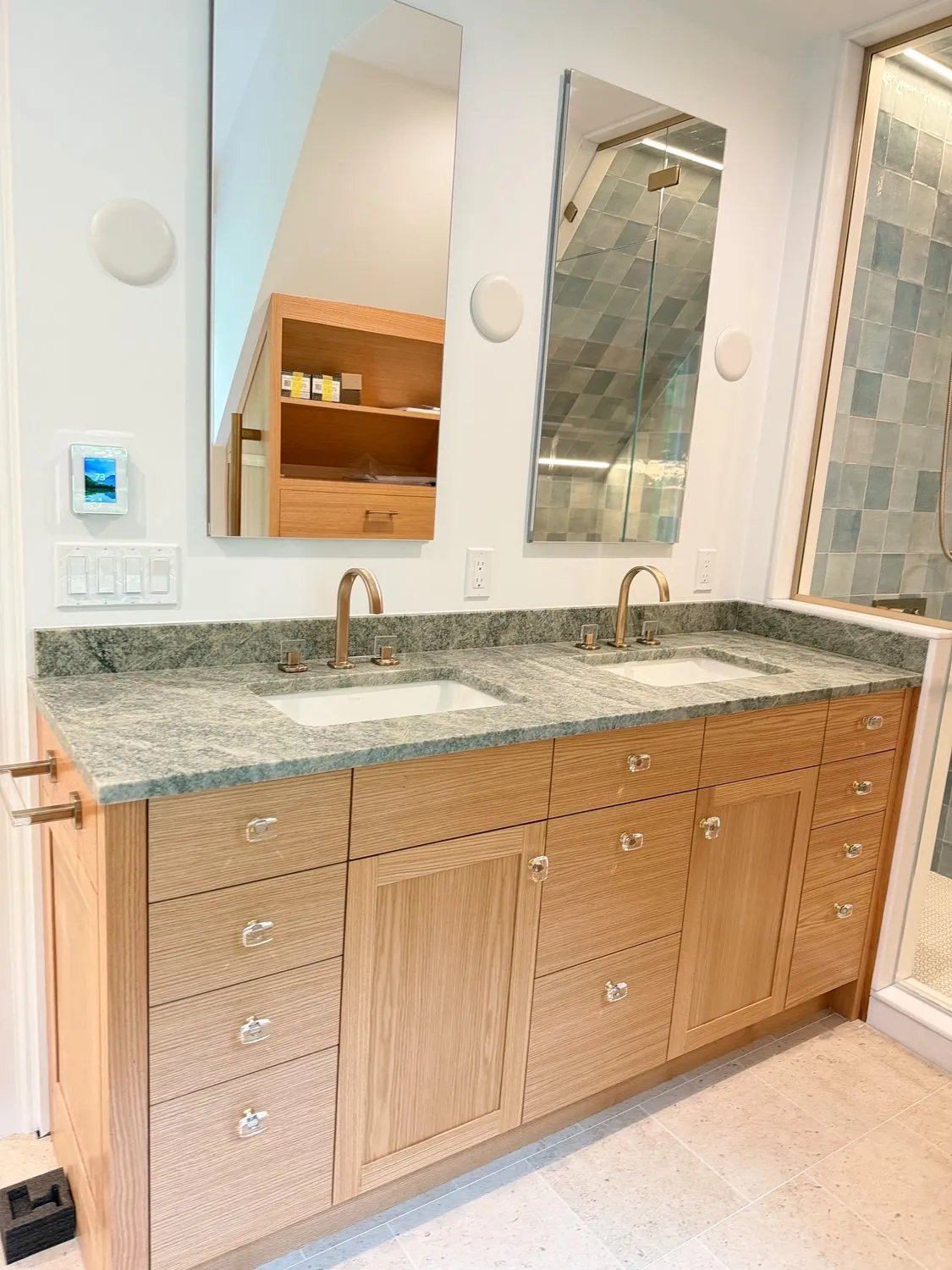 A bathroom with a wood vanity, stone counter and a tiled shower enclosure