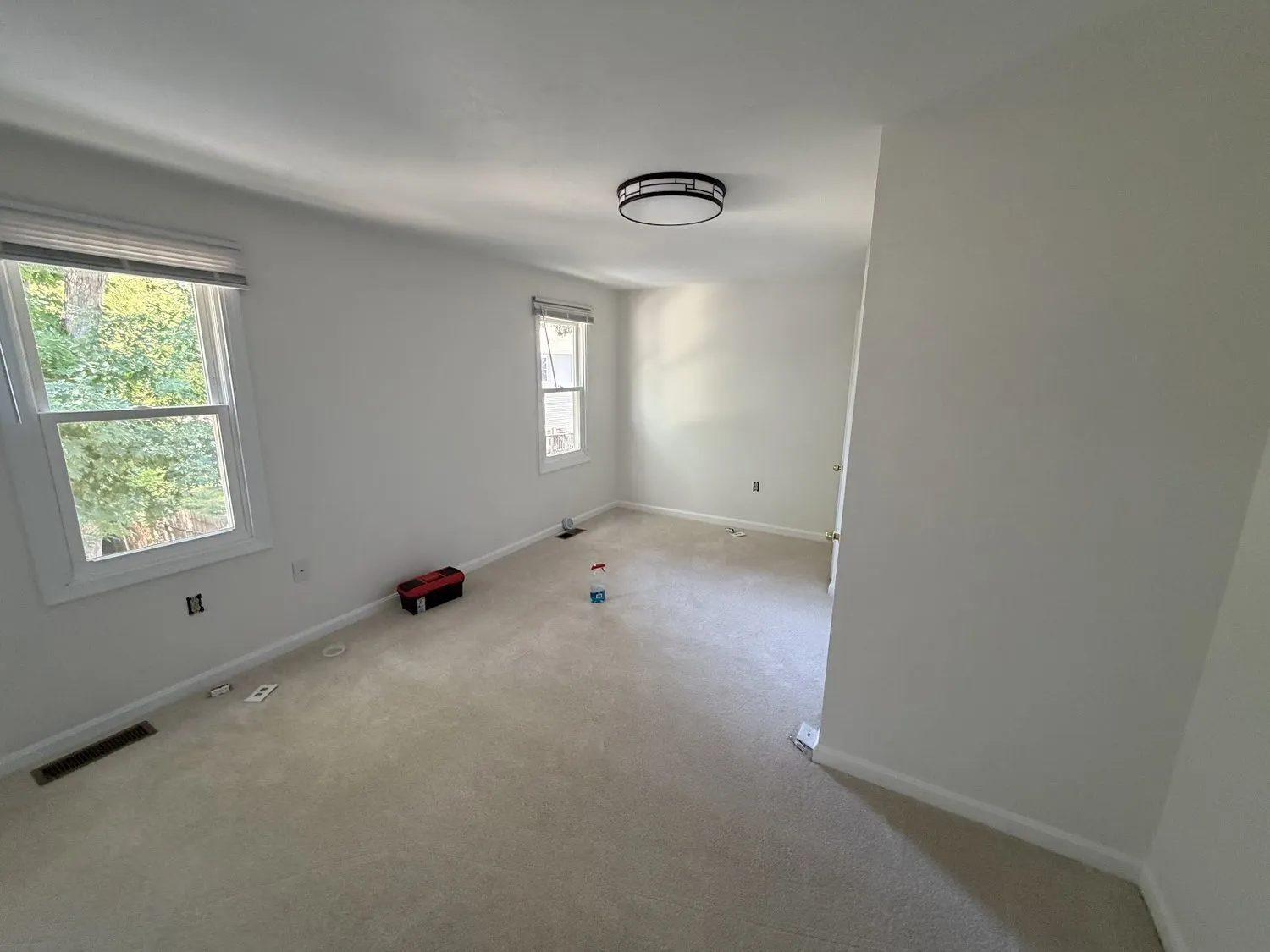 An empty bedroom painted white with a single window and pale carpet