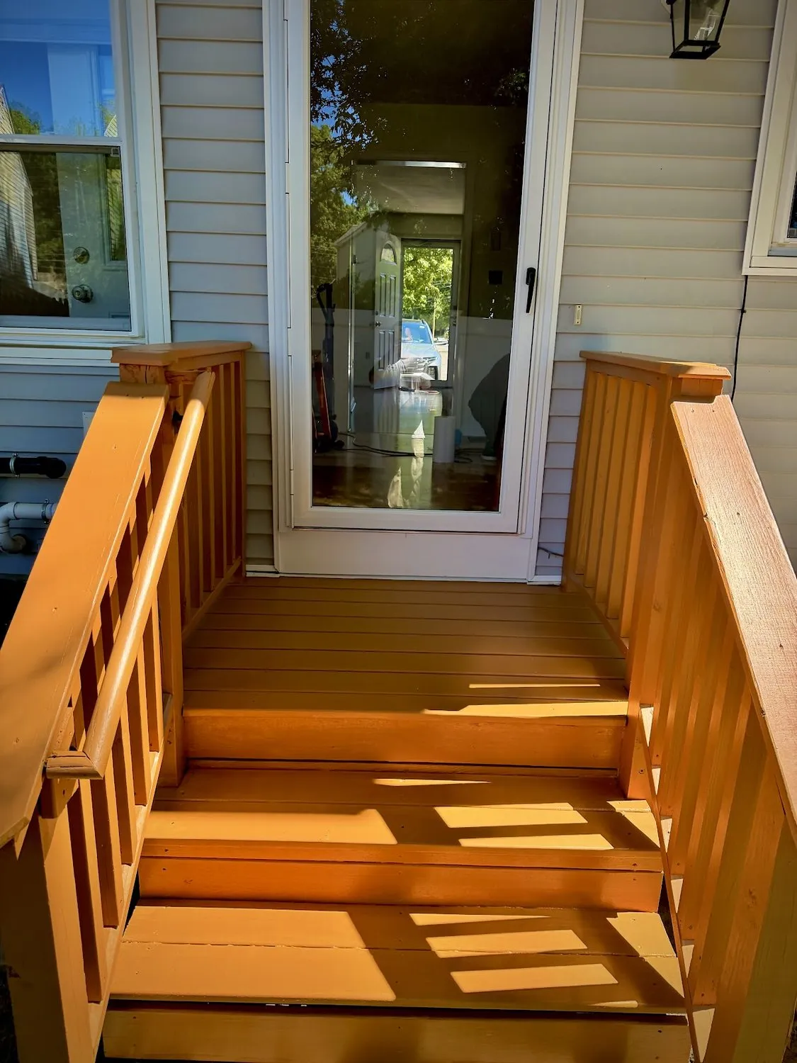 A covered porch with freshly finished wood steps and handrails against white clapboard siding