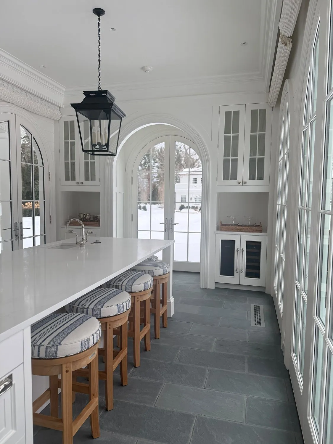 A white kitchen seen through an arched opening, with a lantern pendant and a slate tile floor