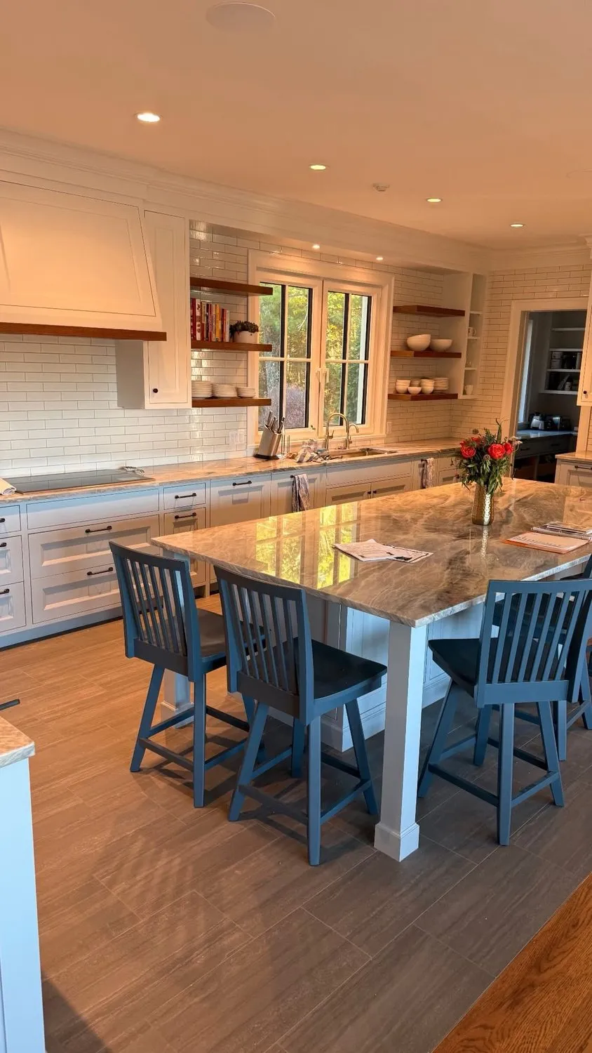 A kitchen island with blue counter stools, white cabinetry and open shelving