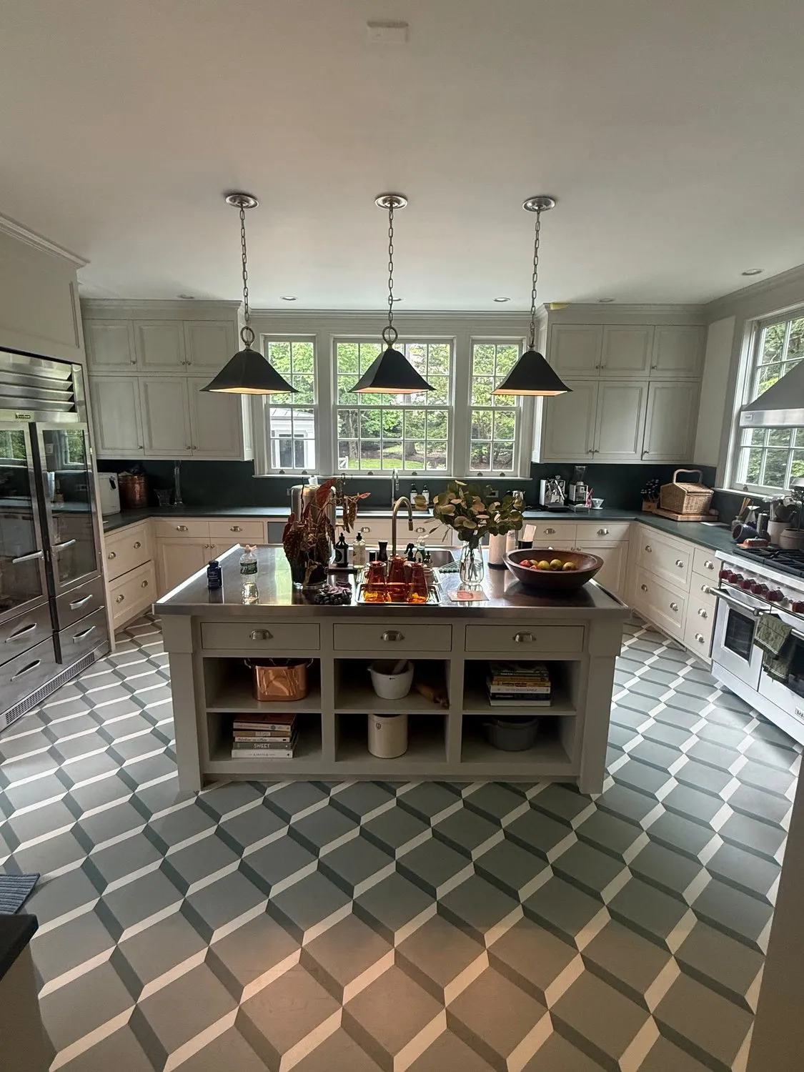 A finished kitchen with pale cabinets, a dark island, pendant lights and a geometric patterned floor