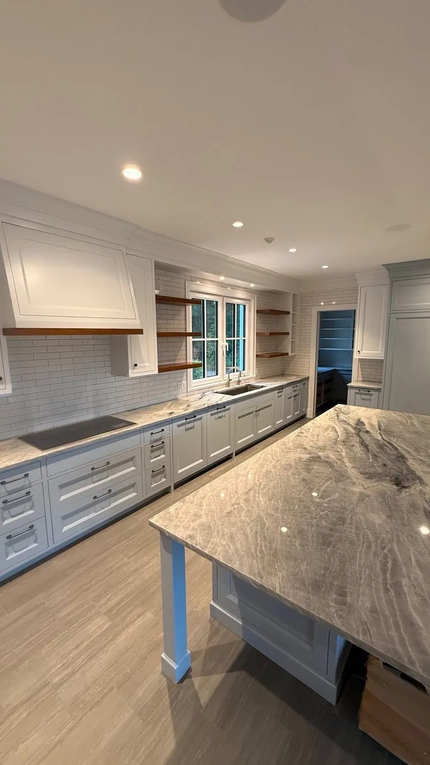 A kitchen with a marble island, white cabinets and a pale tiled backsplash