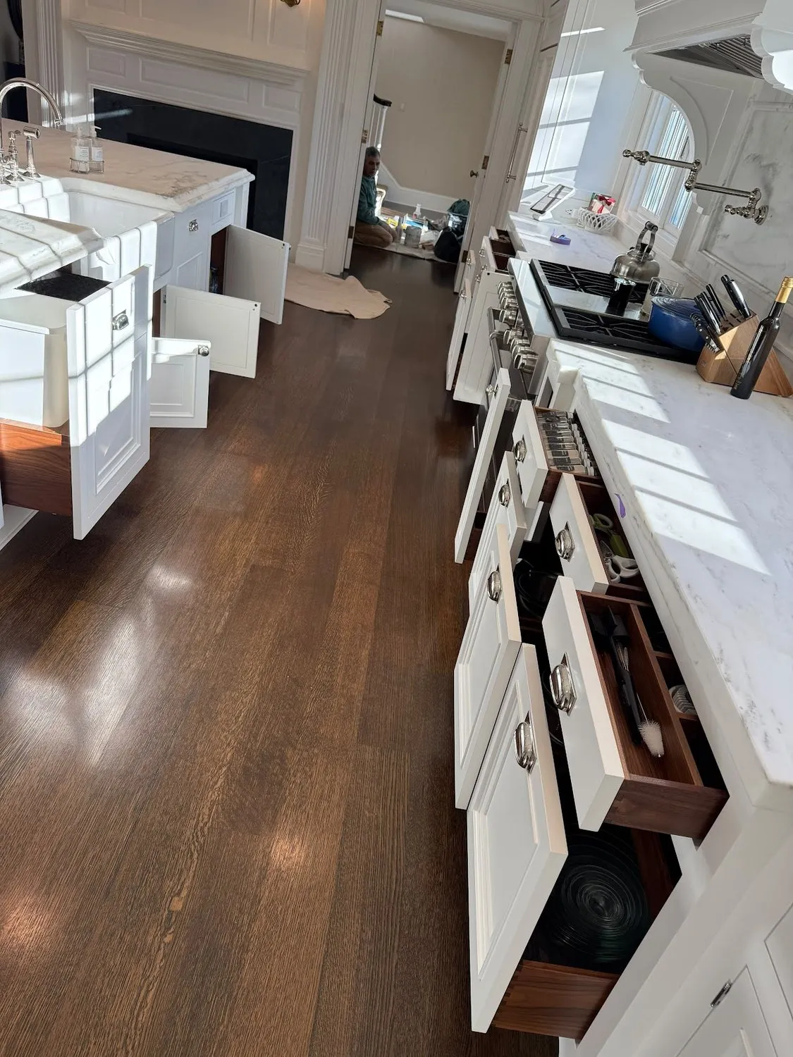 An open-plan kitchen with white cabinetry and dark hardwood floors