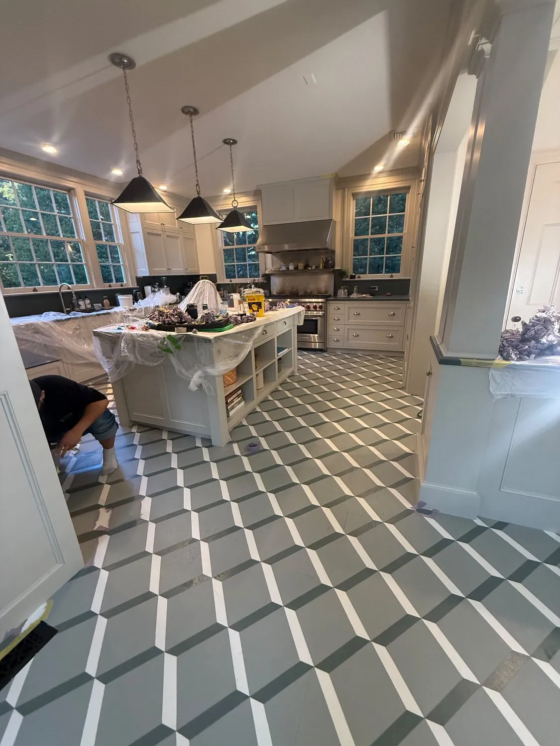 A wide view of a kitchen mid-job, with a geometric patterned floor and pendant lights over the island