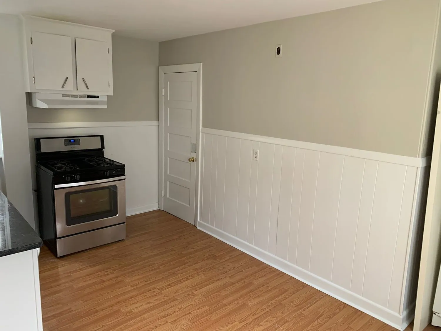 A kitchen with white upper cabinets, white wainscot paneling and a stainless range