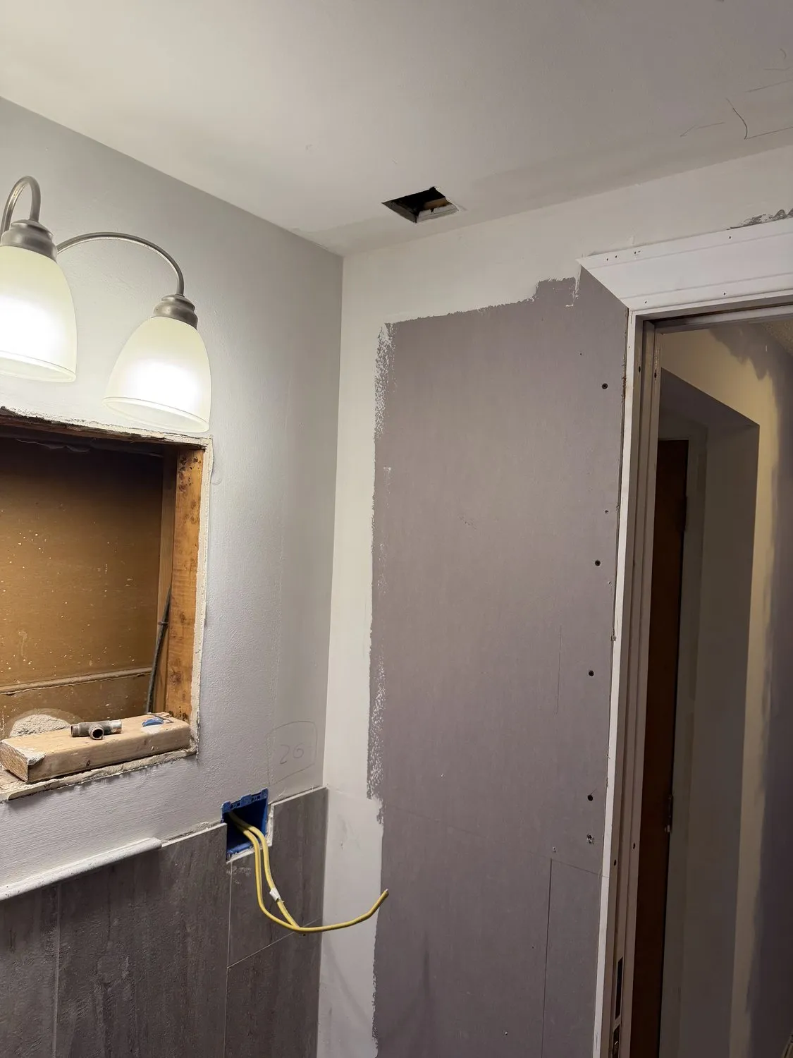 A Norwood bathroom mid-remodel before painting, with a new drywall panel, open wiring and an empty cabinet recess